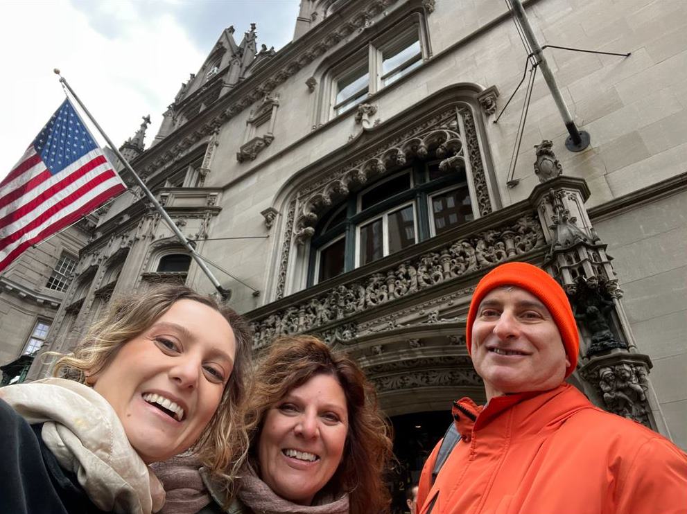 Jared guiding private tour in NYC with two ladies with historic building and American flag in background