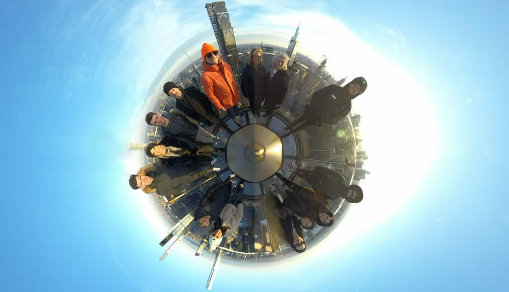 Jared with a tour group at the Top Of The Rock, Rockefeller Center in a 360 degree photo fro above with the NYC skyline behind them.